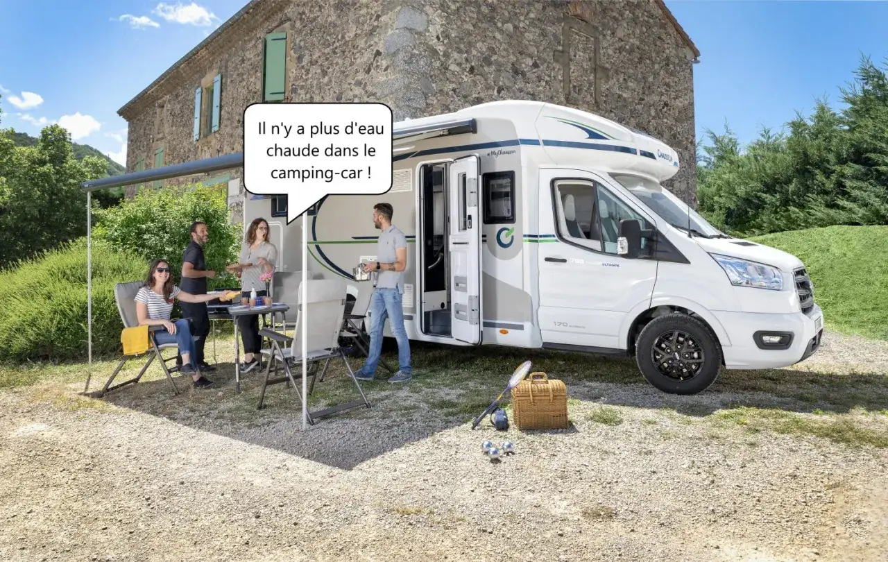 Un camping-car blanc est garé devant une maison en pierre. Une famille est assise à une table à l'extérieur. Le lit électrique est bloqué.