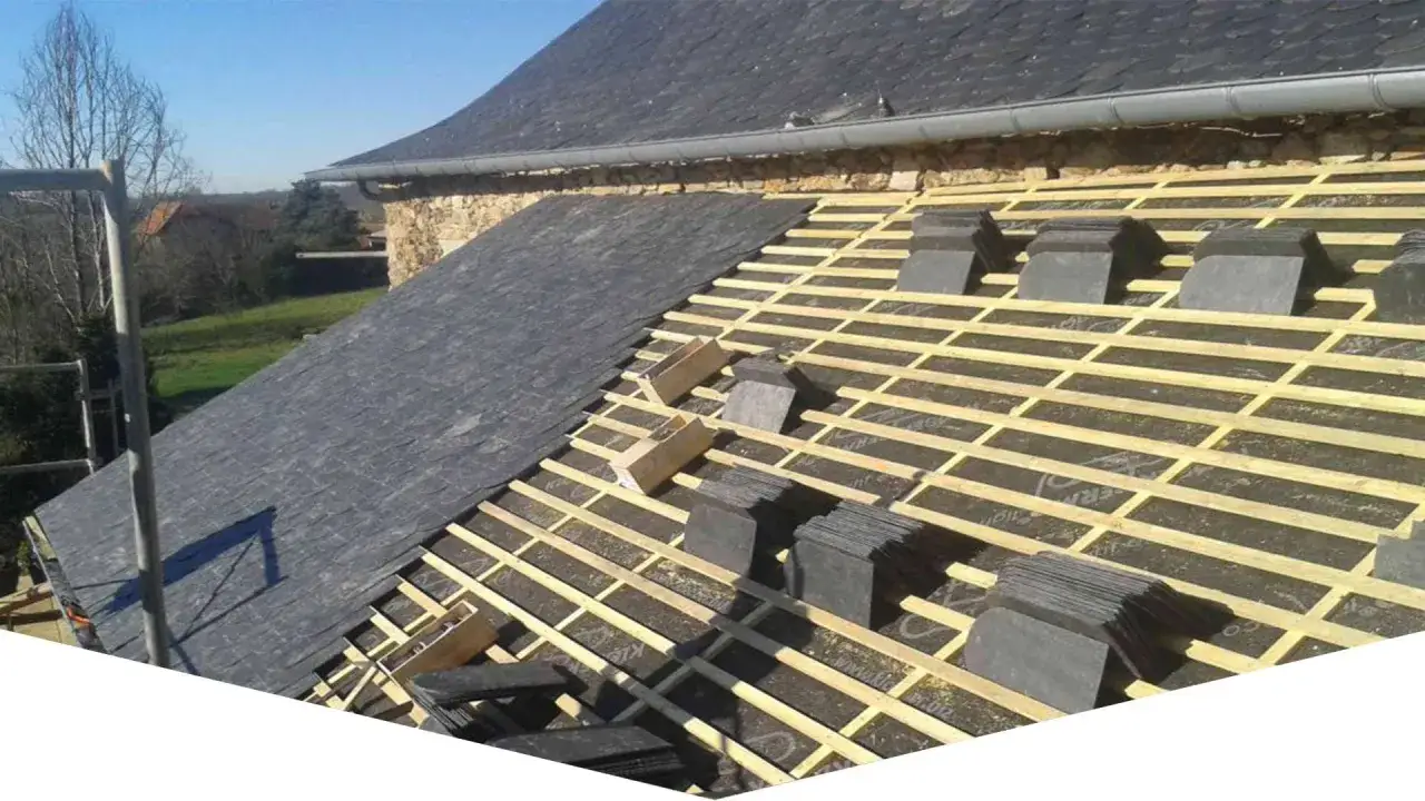 Chantier de toiture ardoise en cours. Des ardoises sont posées sur une partie, tandis que la structure en bois attend les prochaines.