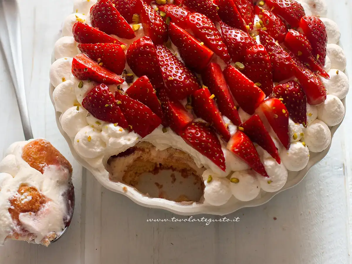 Delizioso tiramisù alle fragole, con panna montata, fragole fresche e pistacchi. Una fetta è già stata servita.