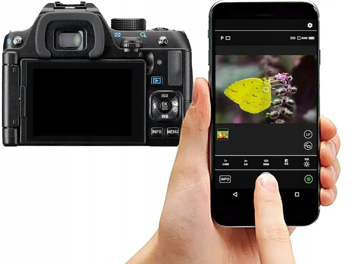 Tył lustrzanki Pentax KM obok smartfona sterującego aparatem. Na ekranie telefonu zdjęcie ż&oacute;łtego motyla.