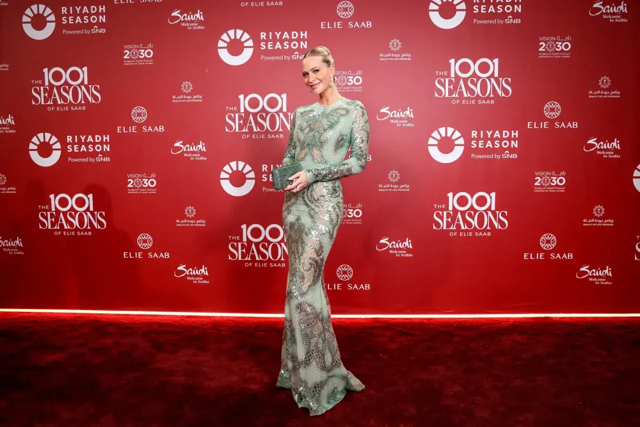 A woman in a sparkling green gown poses on a red carpet at an event celebrating