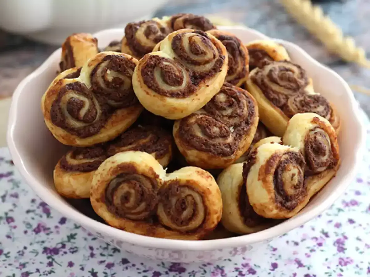 Un tazón lleno de deliciosas palmeras de chocolate, con sus espirales de masa hojaldrada y cacao, listas para ser disfrutadas.