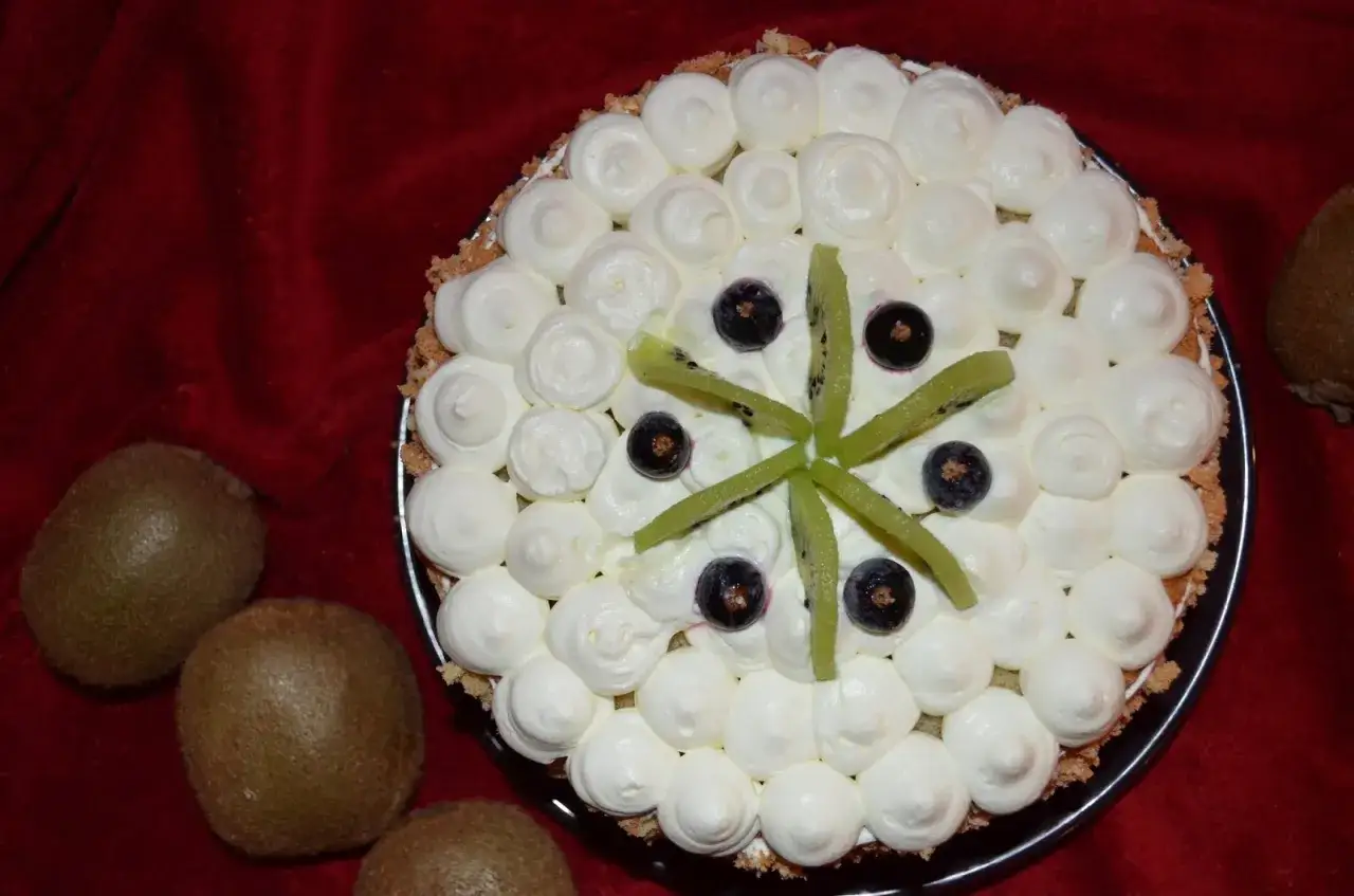 Tort z bitą śmietaną i dekoracjami z kiwi, ozdobiony bor&oacute;wkami. Kiwi tworzy wz&oacute;r gwiazdy na wierzchu.