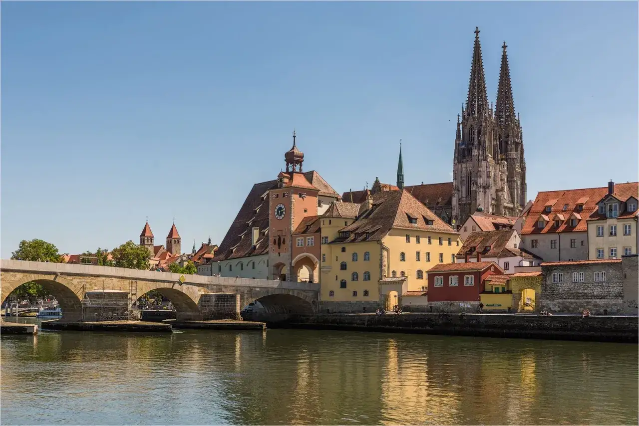 Die Donau flie&szlig;t an Regensburg vorbei, mit der Steinernen Br&uuml;cke und dem Dom Regensburg im Hintergrund.