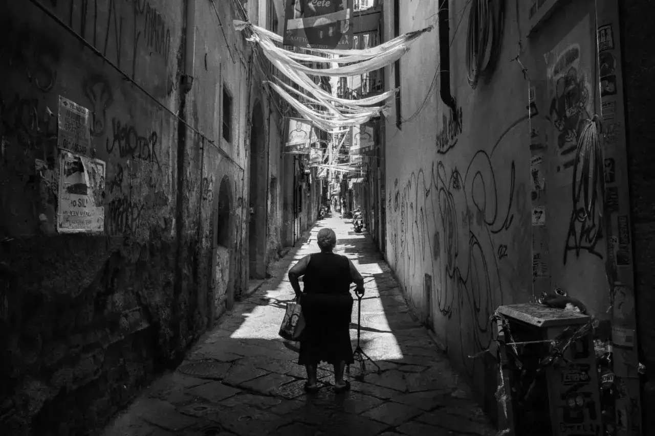 Starsza pani z laską idzie wąską, graffiti-pokrytą uliczką. Klasyczna leica street photo.