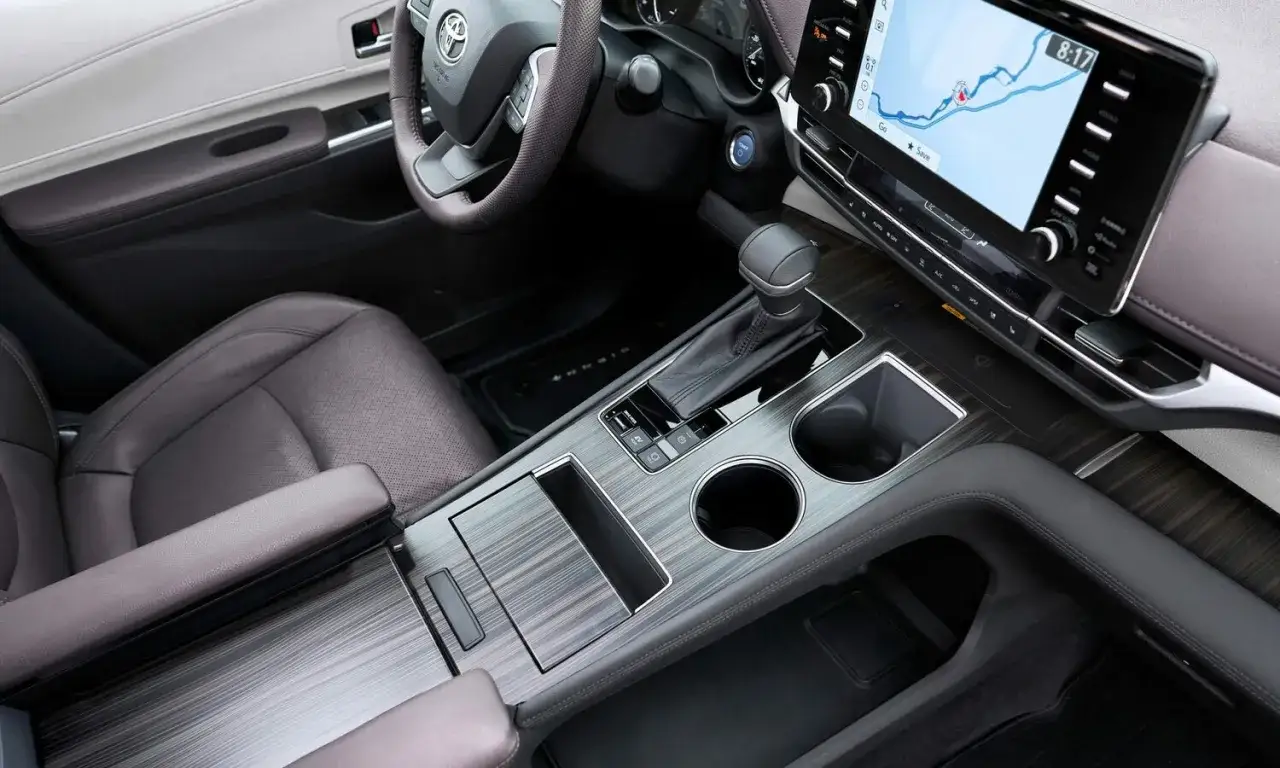 Wnętrze Toyoty Sienny 2025: skórzane fotele, ekran nawigacji, dźwignia zmiany biegów i eleganckie drewniane wykończenie konsoli.