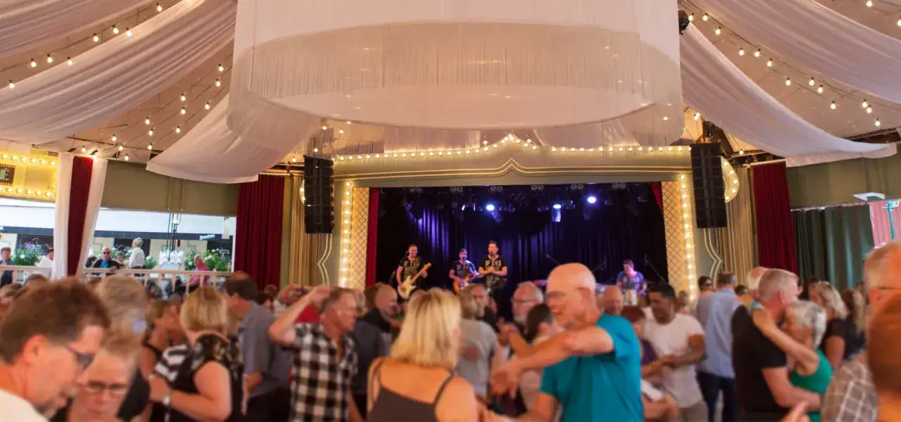 Publik njuter av ett svenskt dansband som spelar på scenen under en festlig tillställning med ljusslingor och draperier.