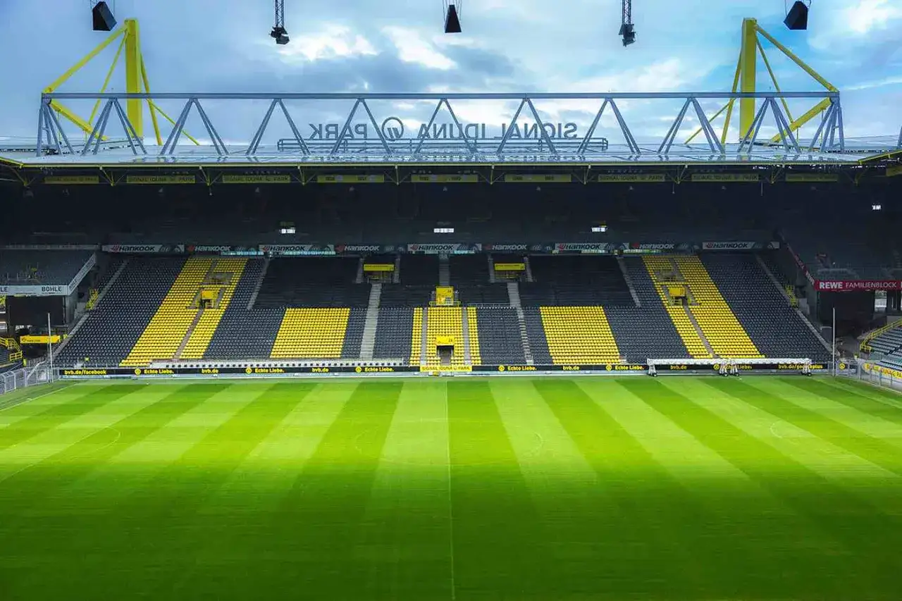 Pusta trybuna stadionu Signal Iduna Park, znana z imponującej pojemności, z zieloną murawą i żółto-czarnymi siedzeniami.