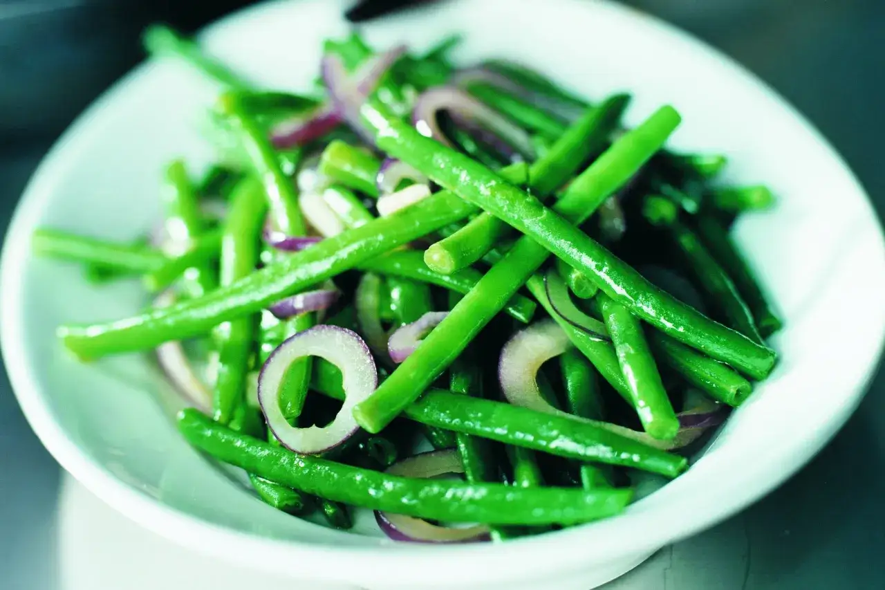En sk&aring;l med fr&auml;scha haricots verts blandade med tunna skivor r&ouml;dl&ouml;k.