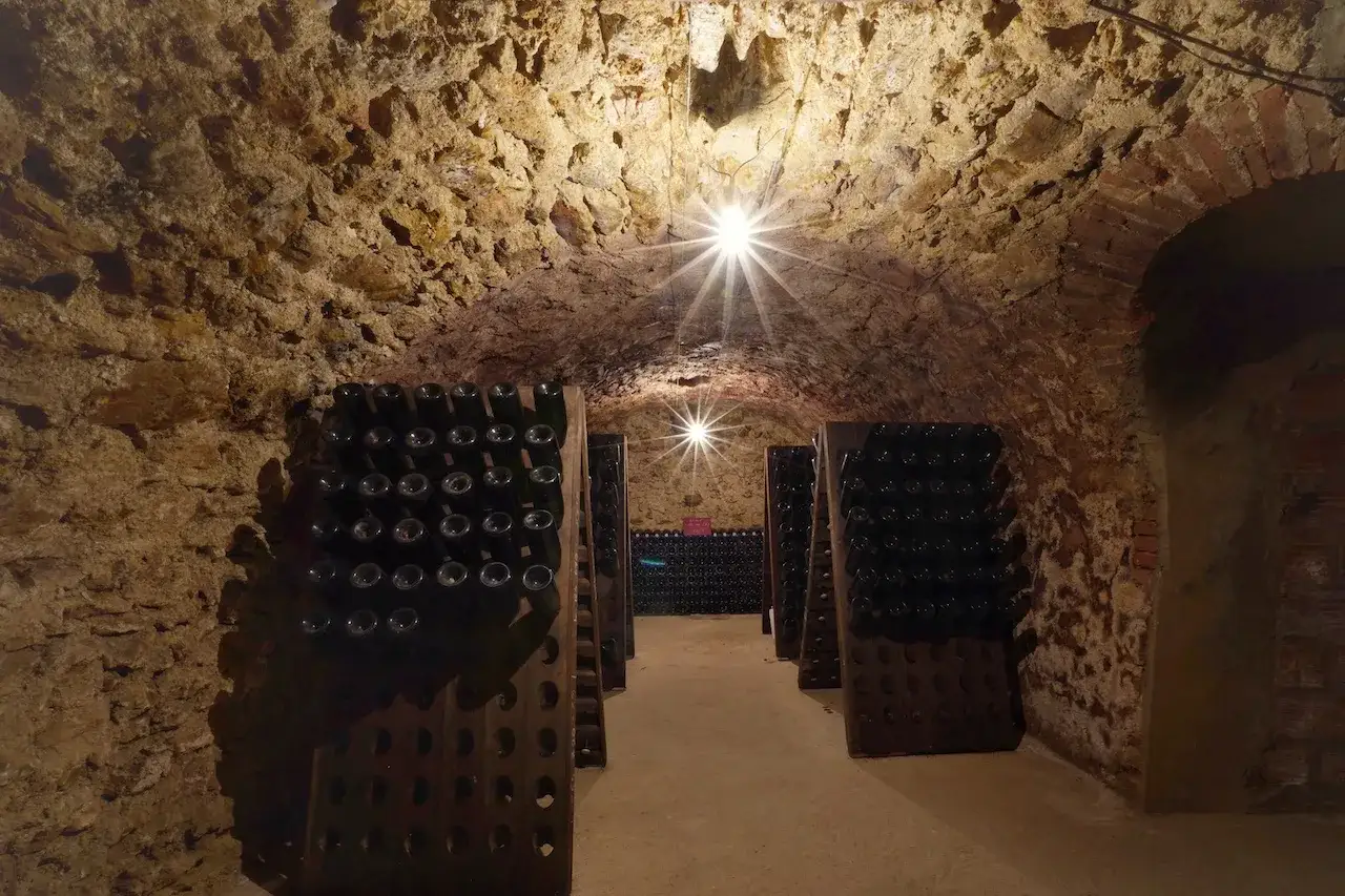 In einer alten Kellergew&ouml;lbe lagern unz&auml;hlige Flaschen Champagner in Holzgestellen. Die dunklen Flaschen warten geduldig auf den perfekten Moment.