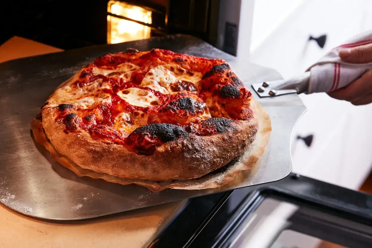 Gorąca, świeżo upieczona pizza z ciągnącym się serem właśnie wyjeżdża z pieca. Idealnie wypieczona, aż chce się ją zjeść!