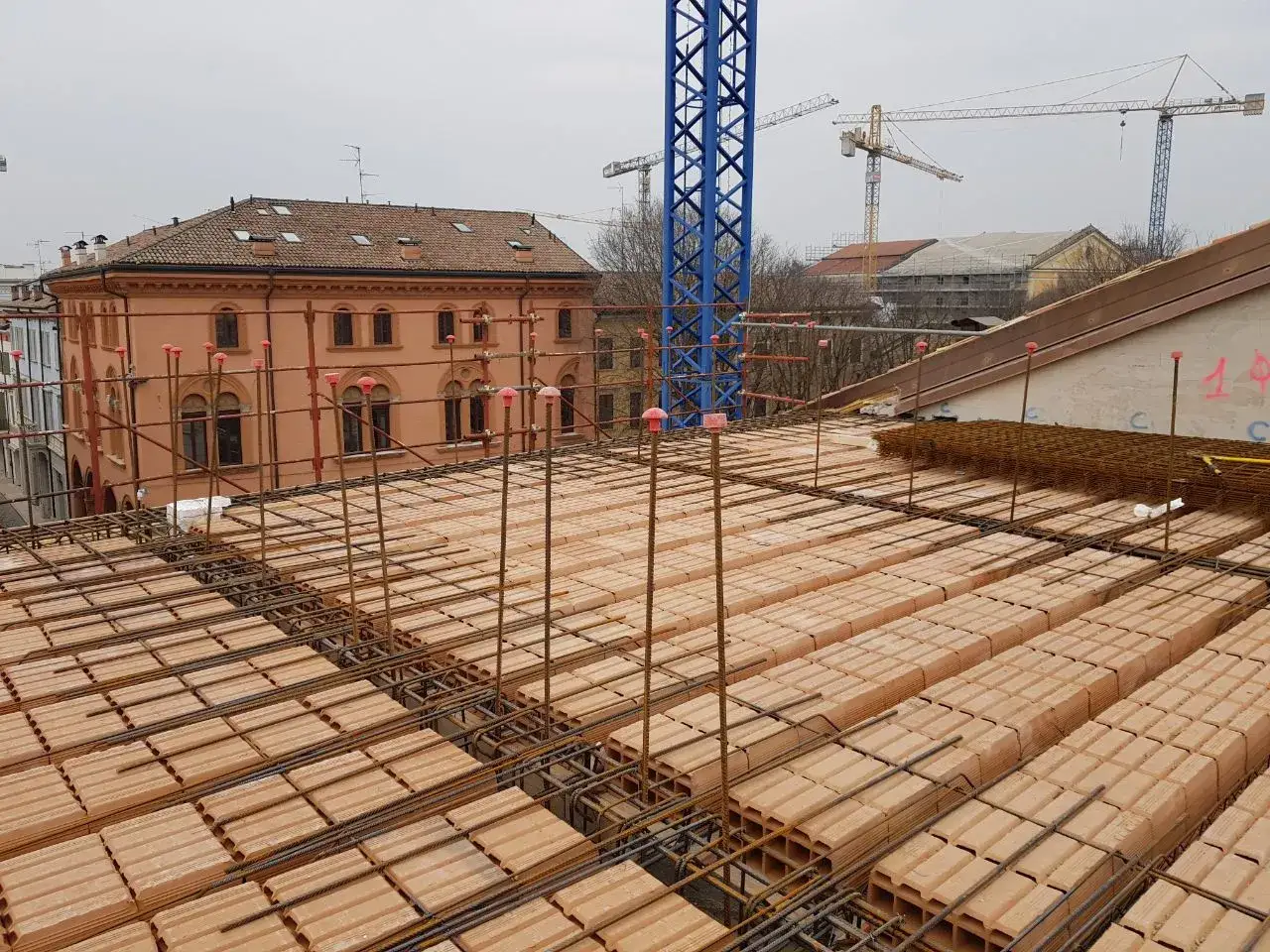 Costruzione di diversi tipi di solaio con mattoni e armature in vista. Gru ed edifici sullo sfondo.