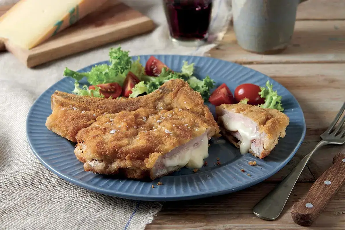 Cotoletta alla Valdostana dorata e croccante, con prosciutto e formaggio filante che cola. Servita con insalata fresca e pomodorini.