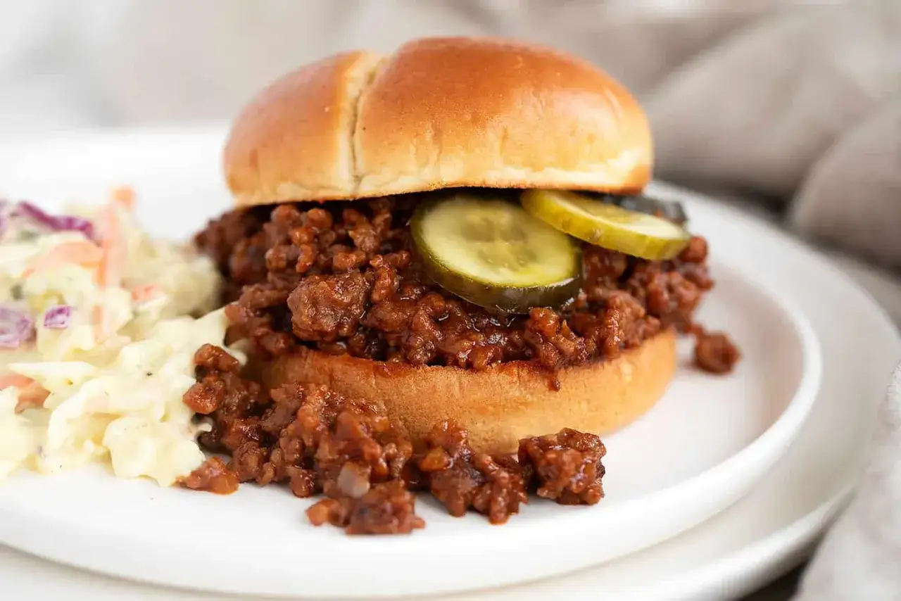 Ein saftiger Sloppy Joe auf einem weichen Br&ouml;tchen, garniert mit Gurkenscheiben, serviert mit cremiger Krautsalat.