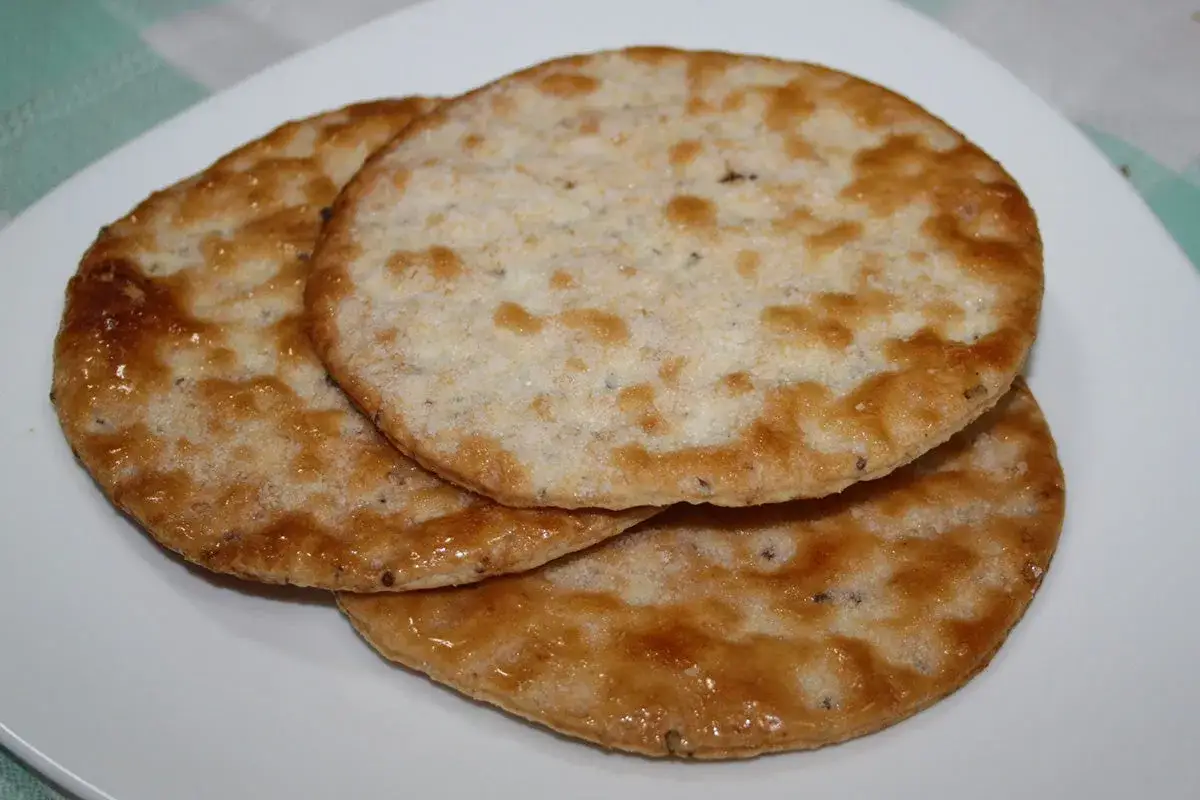 Tres tortas de an&iacute;s doradas y crujientes apiladas en un plato blanco.