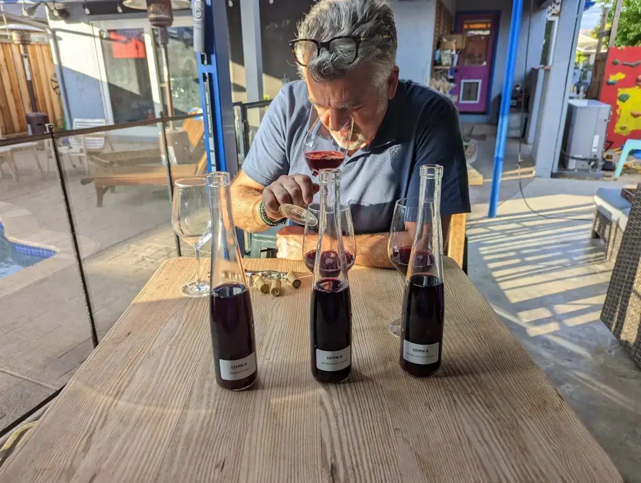 Uomo assaggia vino rosso da bicchiere, con bottiglie e tappi sul tavolo. Chissà quanto guadagna un enologo per un lavoro così raffinato?