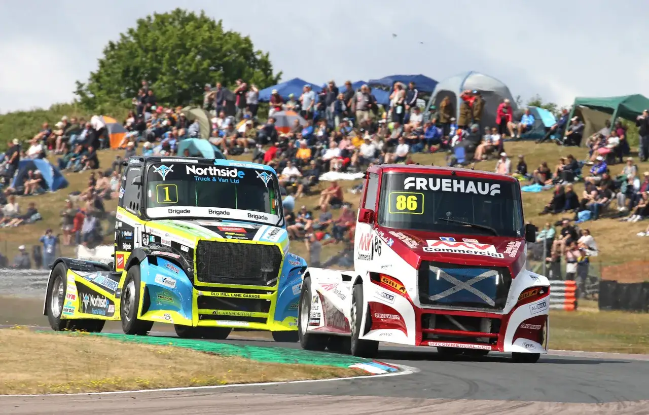 Deux camions de course s'affrontent, atteignant leur vitesse max sur le circuit, sous les yeux d'une foule enthousiaste.
