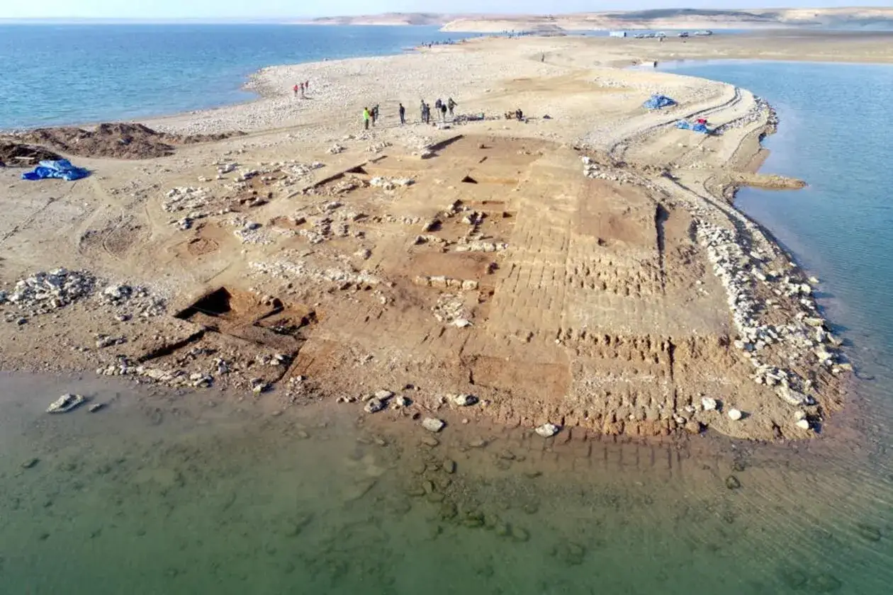 Archeolodzy badają ruiny nad brzegiem rzeki. Widać wykopaliska i kamienne mury.