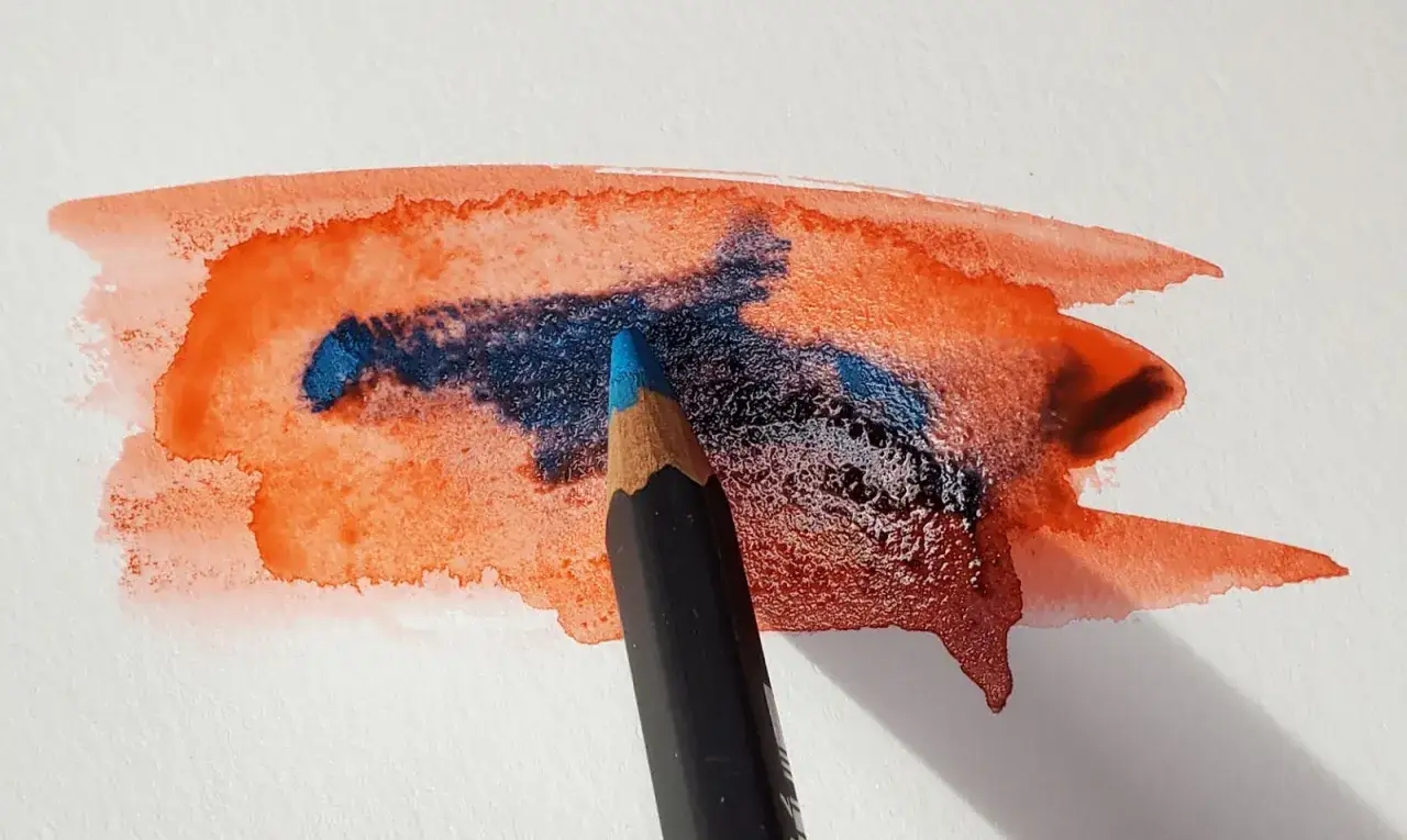 Un crayon aquarelle bleu est utilis&eacute; pour ajouter des d&eacute;tails &agrave; une tache d'aquarelle orange.
