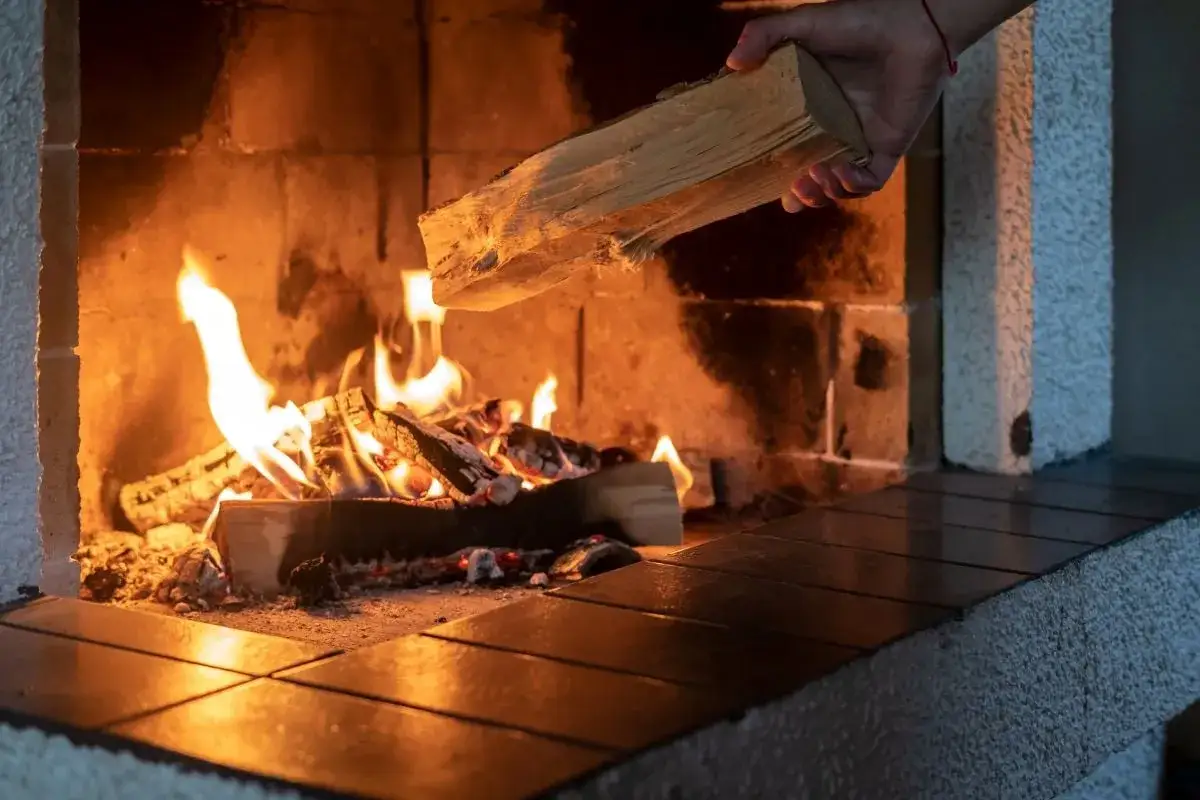 Hand legt Eichenholz ins Feuer. Der hohe Brennwert von Eiche sorgt für langanhaltende Wärme und Gemütlichkeit im Kamin.