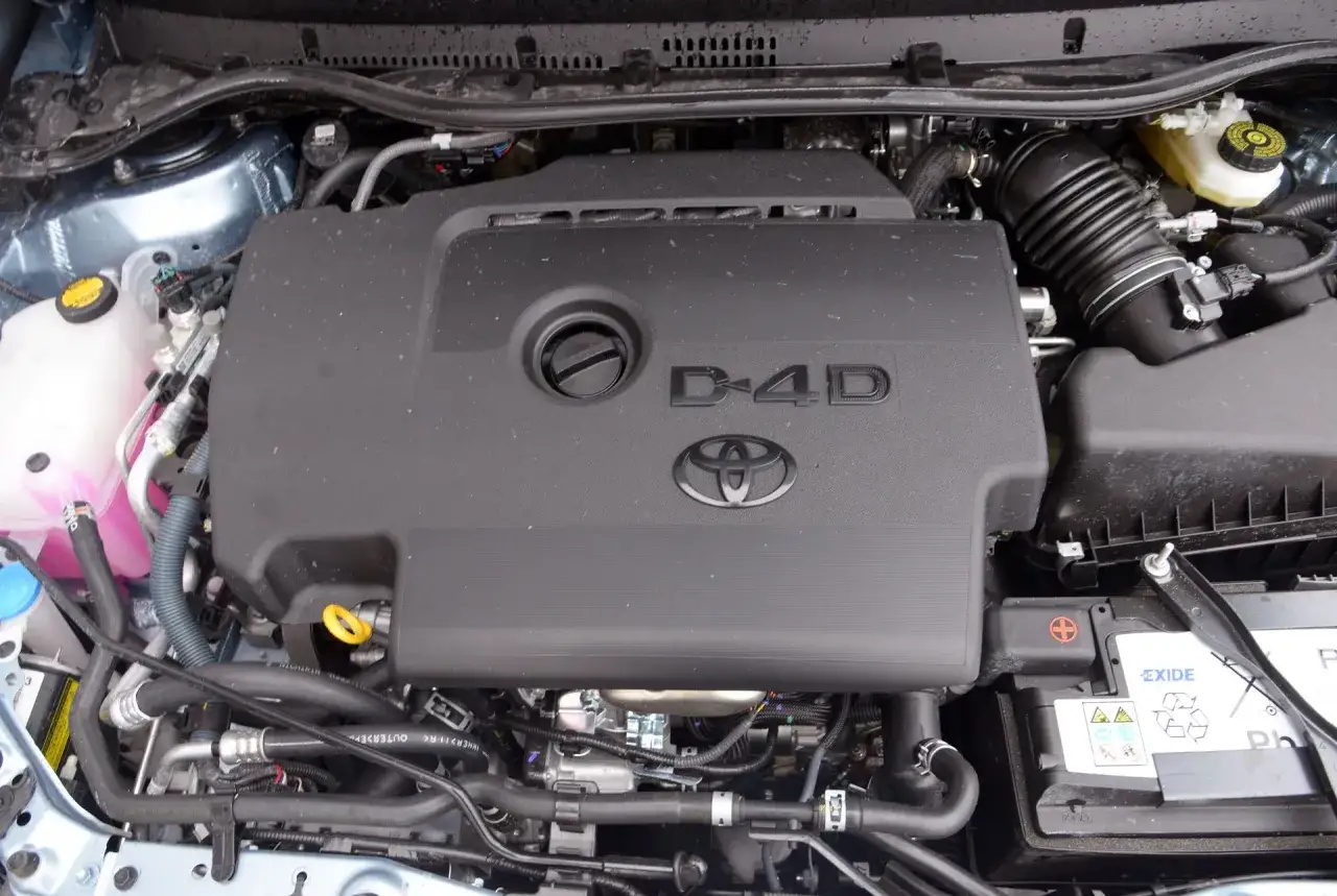 Silnik D-4D w Toyota Auris 2015. Widoczny jest czarny plastikowy dekiel z logo Toyoty i napisem D-4D, a także elementy układu dolotowego i akumulator Exide.