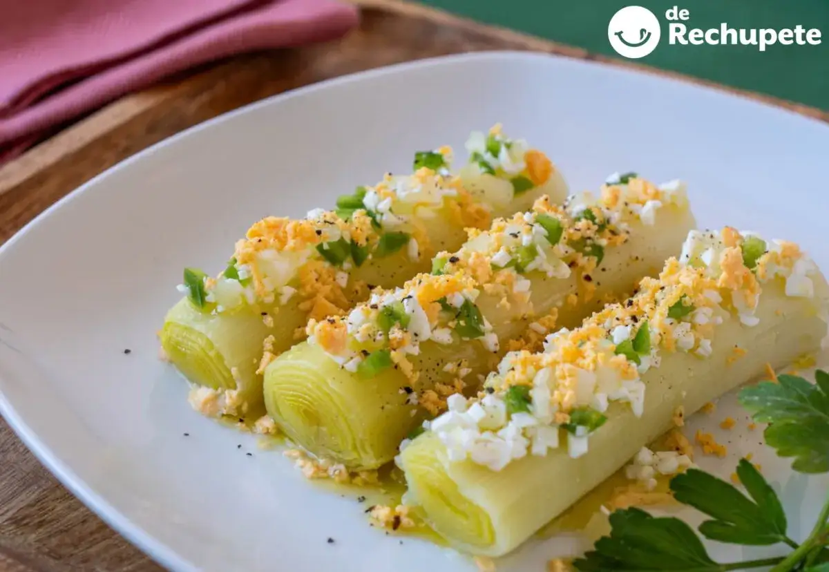 Puerros cocidos cubiertos con huevo duro picado y pimiento verde. Una idea deliciosa para tus recetas con puerros.