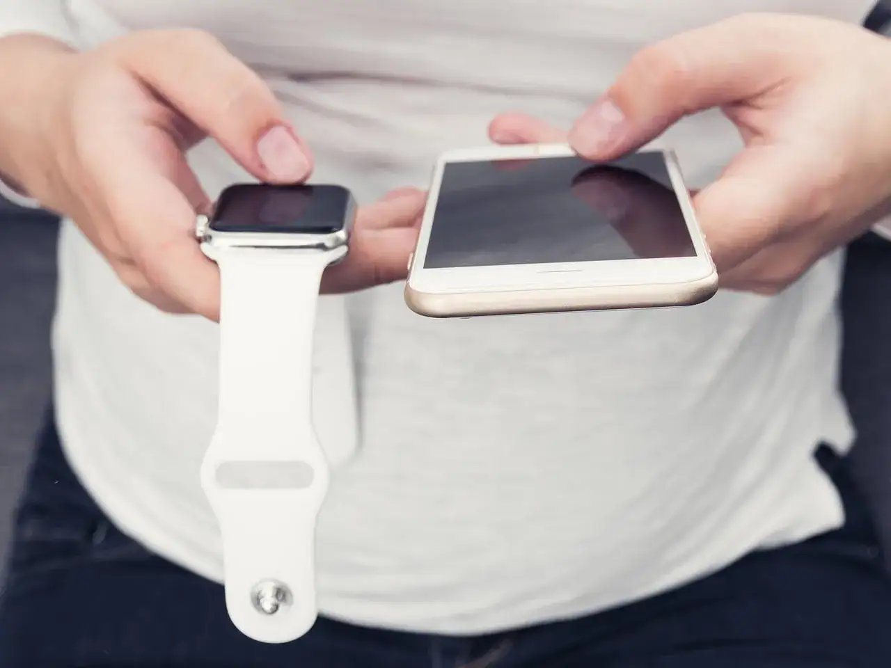 Dłonie trzymają smartwatch i smartfon. Co zrobić, gdy smartwatch nie chce się włączyć? Sprawdź połączenie z telefonem.