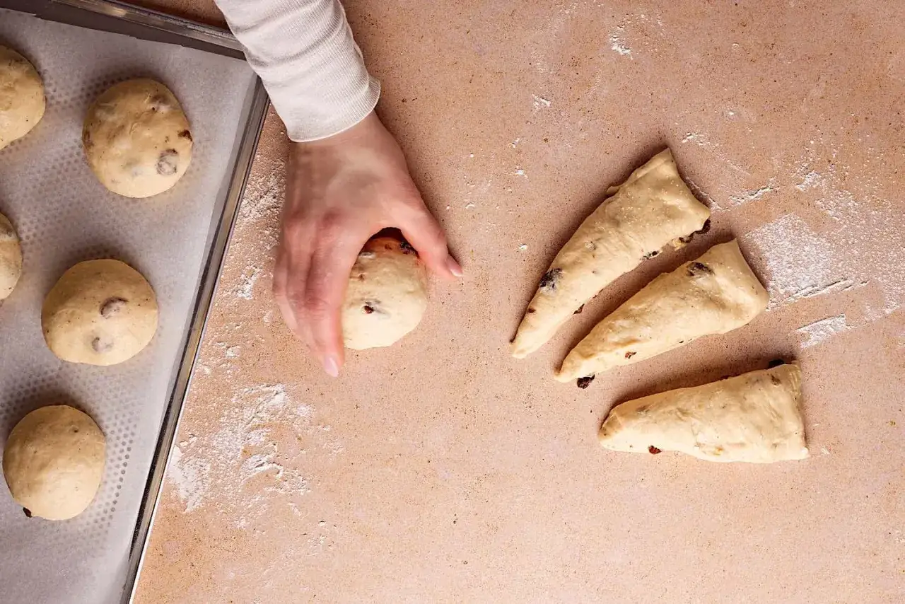 Hand formt Teig für kleines Brot backen. Auf Blech liegen bereits geformte Teiglinge. Daneben liegen weitere Teigstücke.