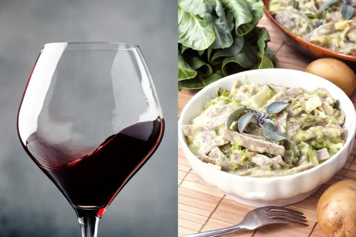 Un bicchiere di vino rosso, perfetto vino da abbinare ai pizzoccheri, accanto a un piatto fumante di questa specialità valtellinese.