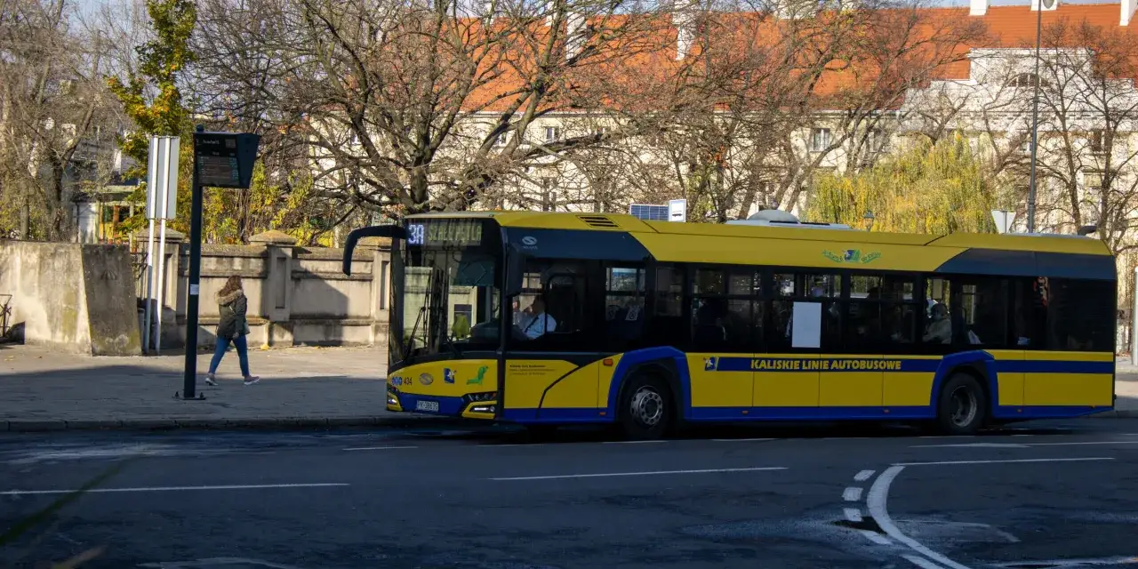 Żółty autobus Kaliskich Linii Autobusowych zatrzymuje się przy przystanku, gdzie widać rozkład jazdy autobusów Kalisz.