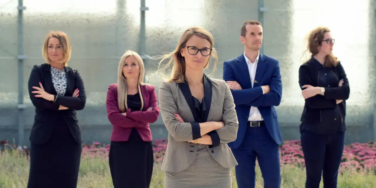 Zespół profesjonalistów w garniturach stoi z założonymi rękami przed nowoczesnym budynkiem.