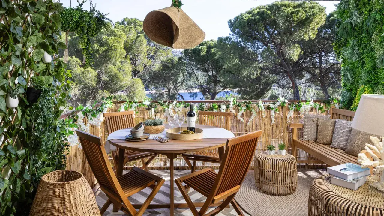 Ideas para decorar una terraza: mesa de madera, sillas, banco, plantas y un sombrero colgando.