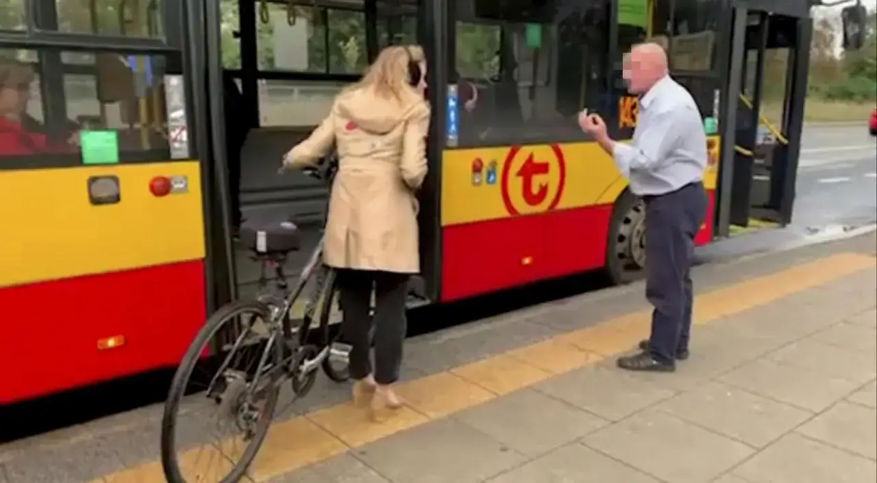 Kobieta z rowerem wchodzi do autobusu. Mężczyzna stoi obok.