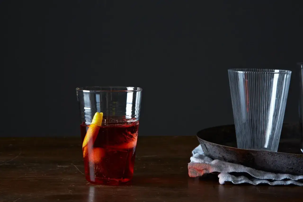 Czerwony koktajl z pomarańczą w szkle, obok puste szklanki. Wybór między Negroni czy Boulevardier.