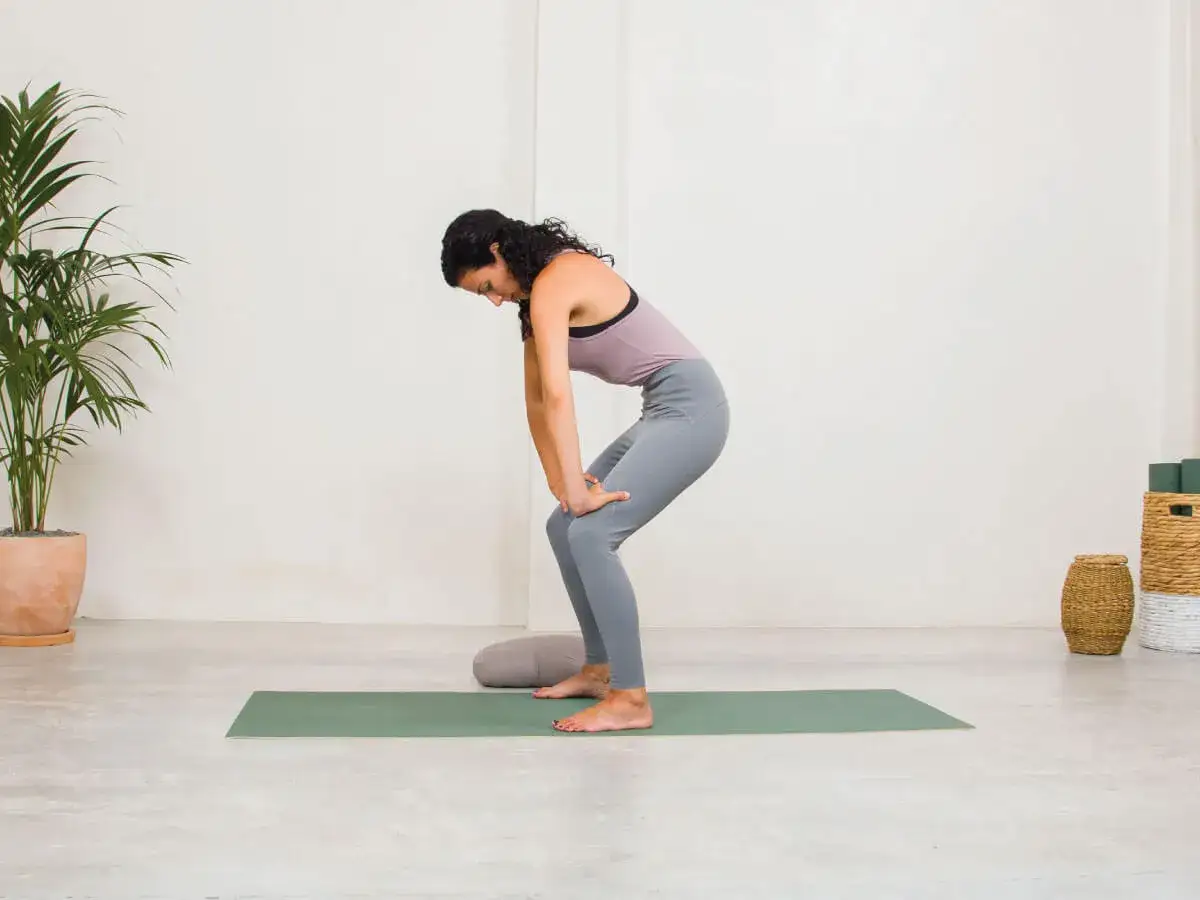 Mujer en postura de yoga, flexionando rodillas y espalda, manos en muslos. Practica el maha bandha.