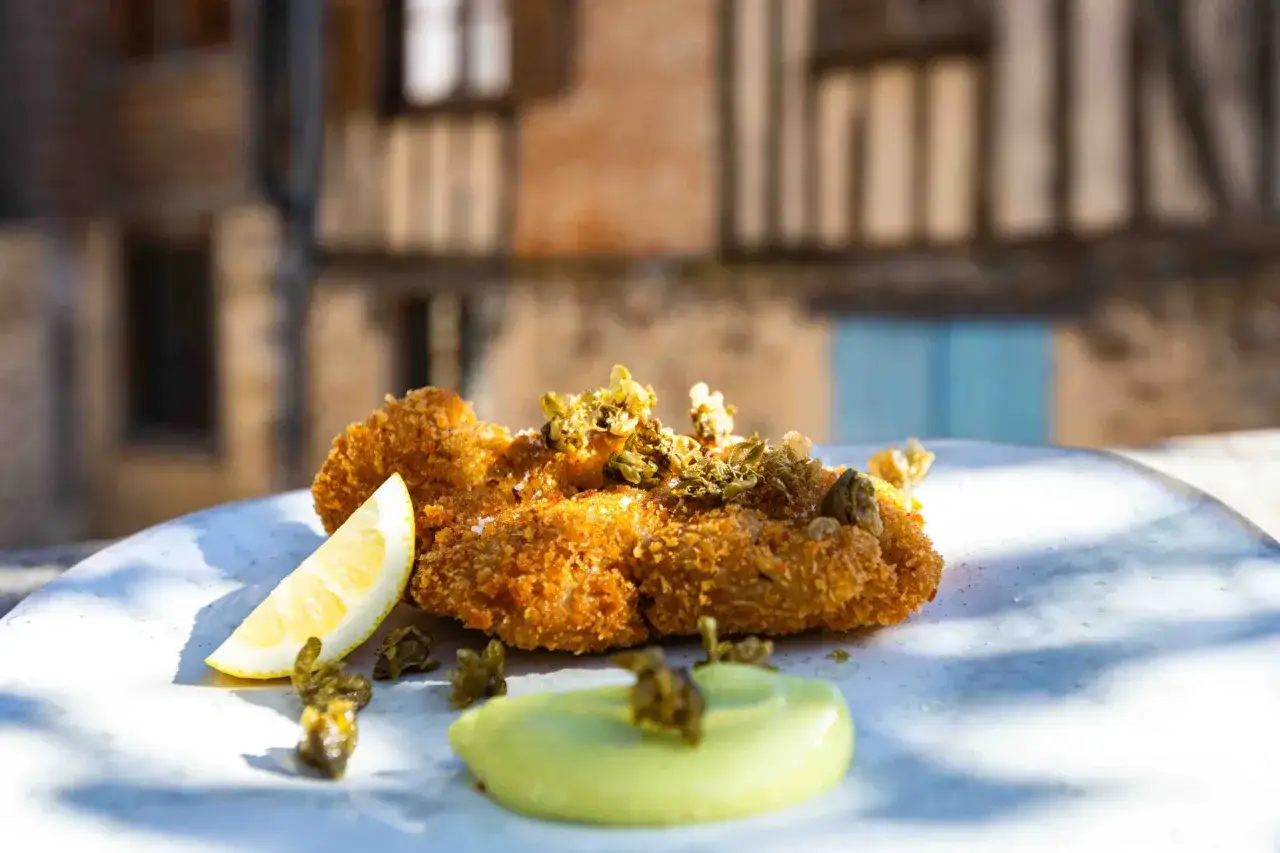 Un plat de ris de veau pané, garni de câpres et accompagné d'une sauce verte et d'un quartier de citron.
