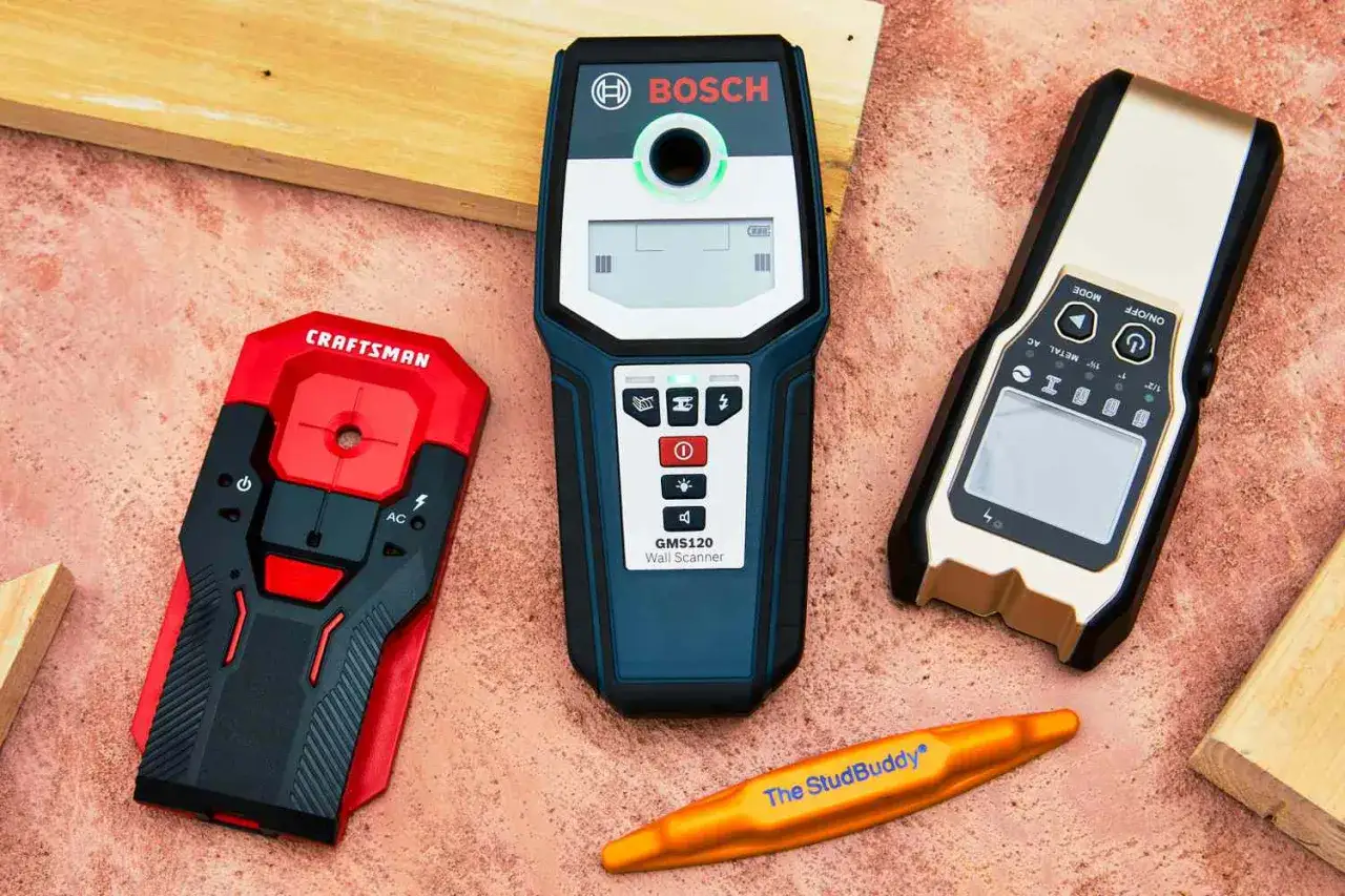 Three stud finders and a StudBuddy tool are laid out, ready to demonstrate how to use a stud finder to locate wall studs.