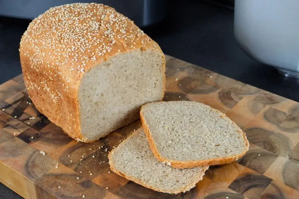 Frisch gebackenes sesam brot mit zwei Scheiben auf einem Holzbrett.