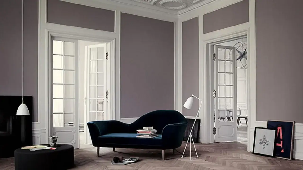 Elegante Wohnzimmer-Ideen: Eine zweifarbige Wandgestaltung in Grau-Violett mit wei&szlig;en Zierleisten und T&uuml;ren schafft Tiefe. Ein tiefblauer Samt-Sofa und moderne Lampen setzen Akzente.