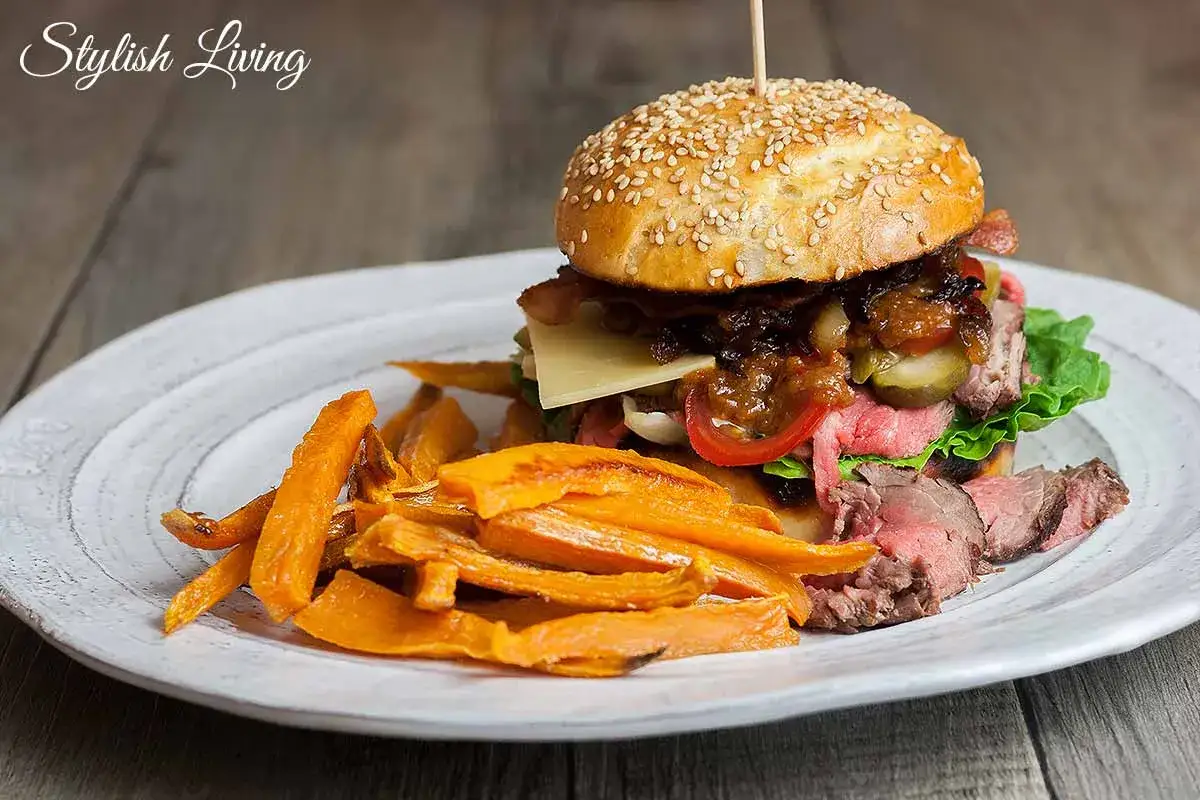 Ein saftiger Hamburger mit zartem Roastbeef, Käse und karamellisierten Zwiebeln, serviert mit knusprigen Süßkartoffel-Pommes.