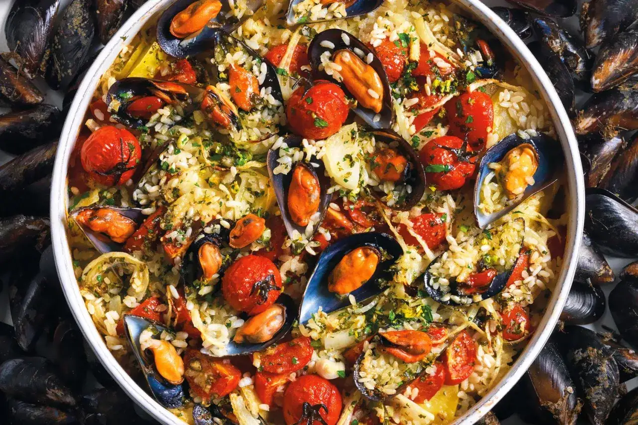 Un saporito riso patate e cozze, con pomodorini e prezzemolo tritato, circondato da cozze fresche.