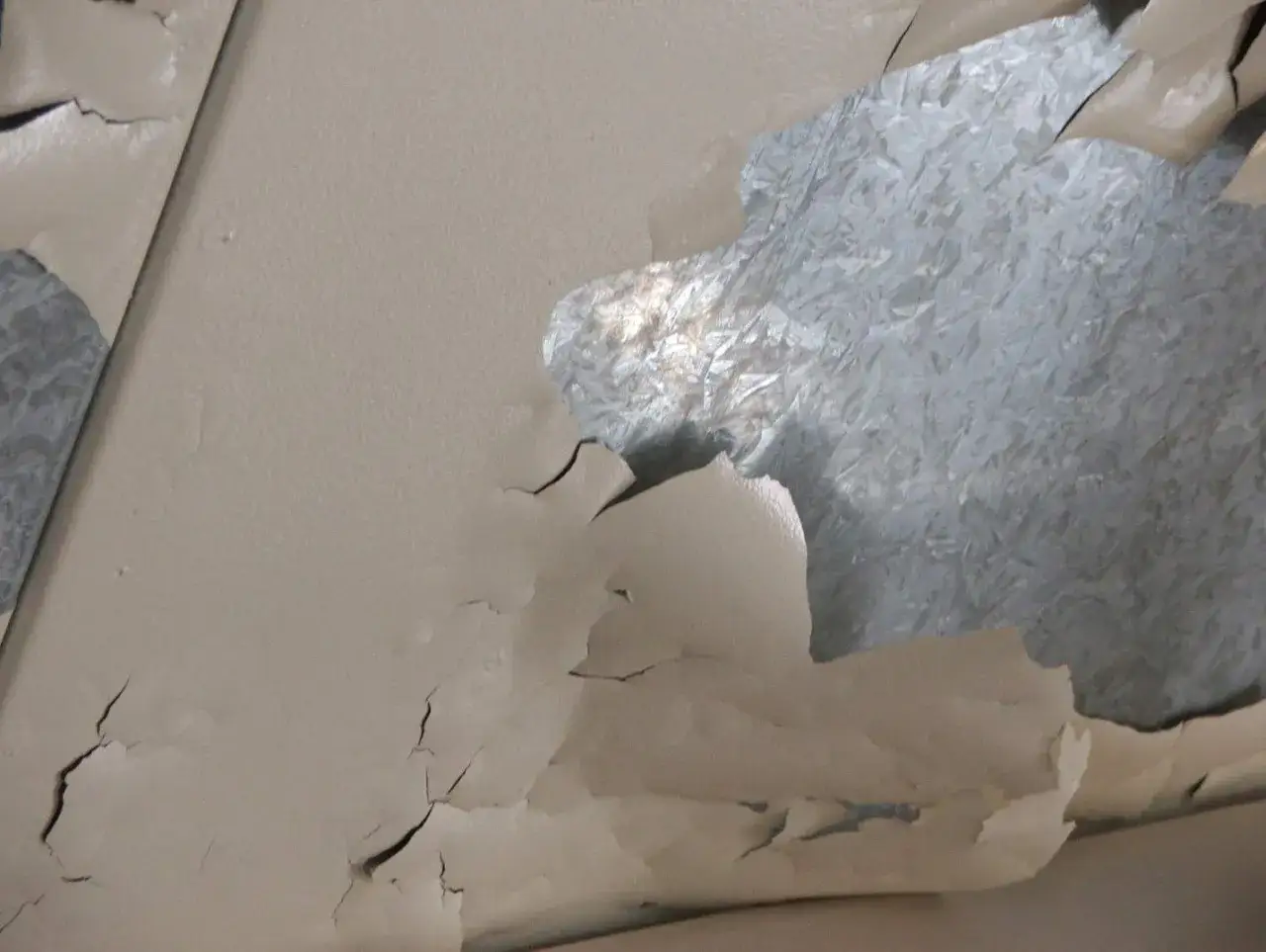 La pintura se desprende de la chapa galvanizada, revelando el metal debajo.