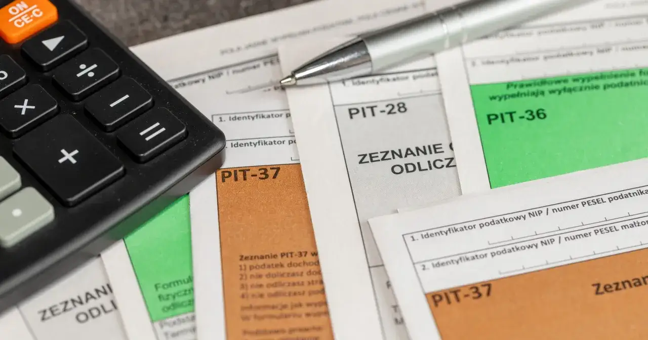 Kalkulator i długopis leżą na dokumentach PIT-37, PIT-28 i PIT-36. Czas na rozliczenie podatku!