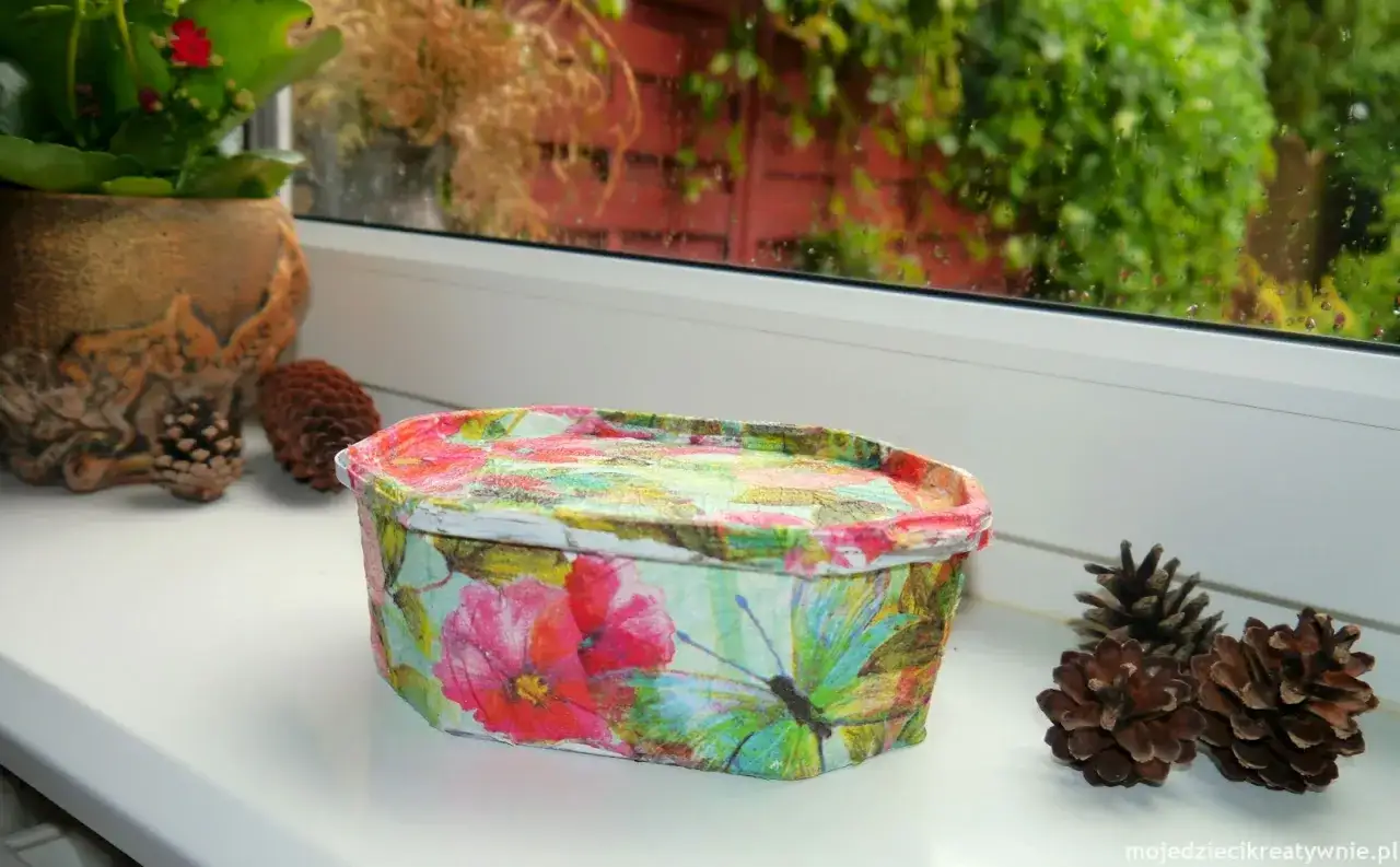 Uroczy koszyczek z motywem kwiatów i motyli, wykonany techniką decoupage na plastiku. Idealny do przechowywania drobiazgów.