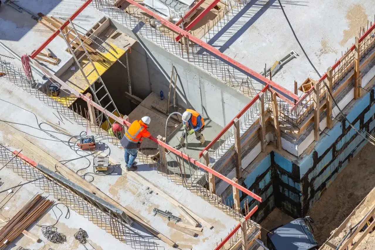 Operai in cantiere, con indumenti ad alta visibilit&agrave;, lavorano alla gettata di cemento. La scena mostra la consulenza tecnica d'ufficio in azione, con attenzione ai dettagli costruttivi.
