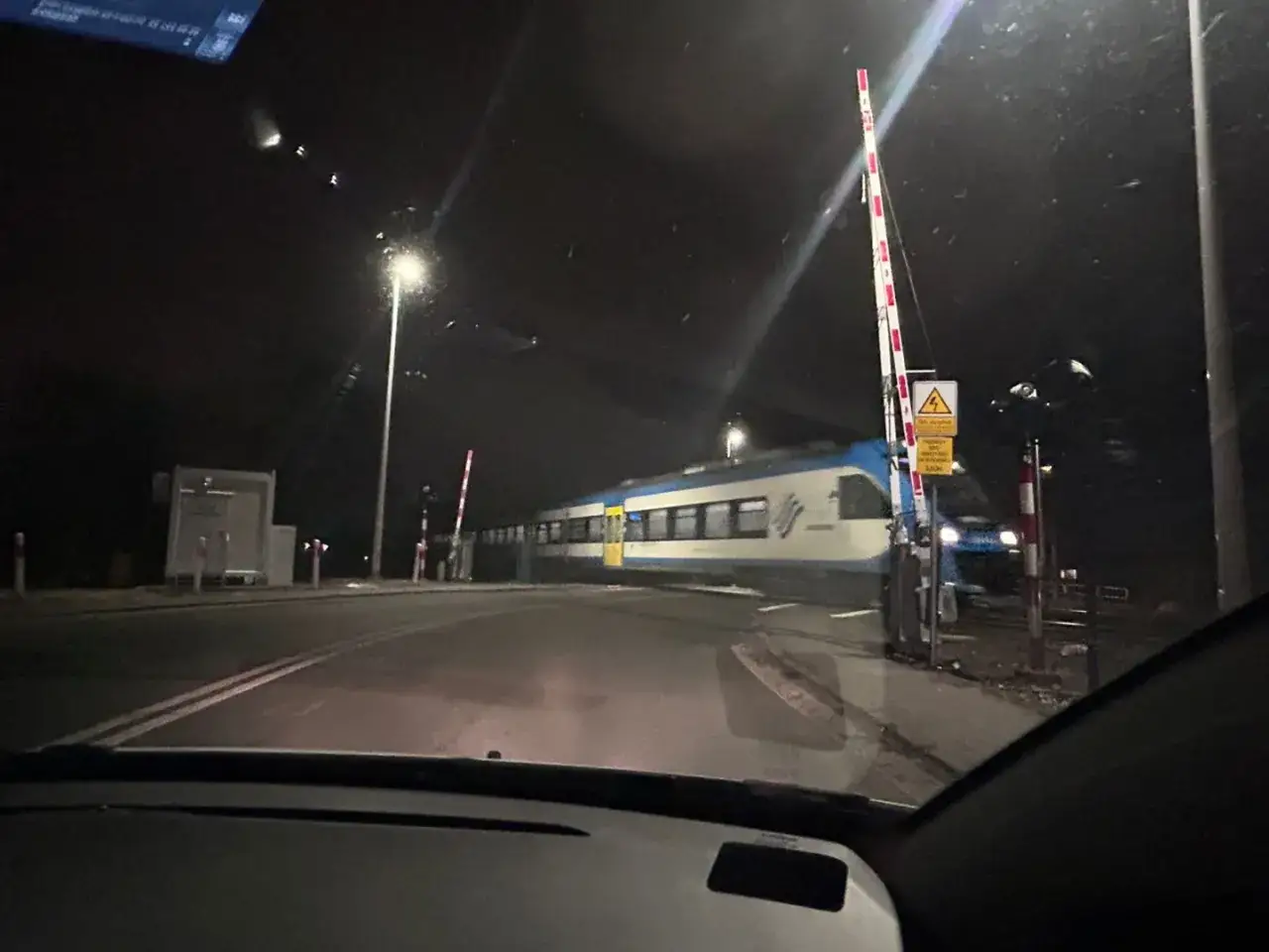 Pociąg PKP Intercity mija przejazd kolejowy nocą. Na słupku ostrzegawczym wisi ż&oacute;łta naklejka PLK.