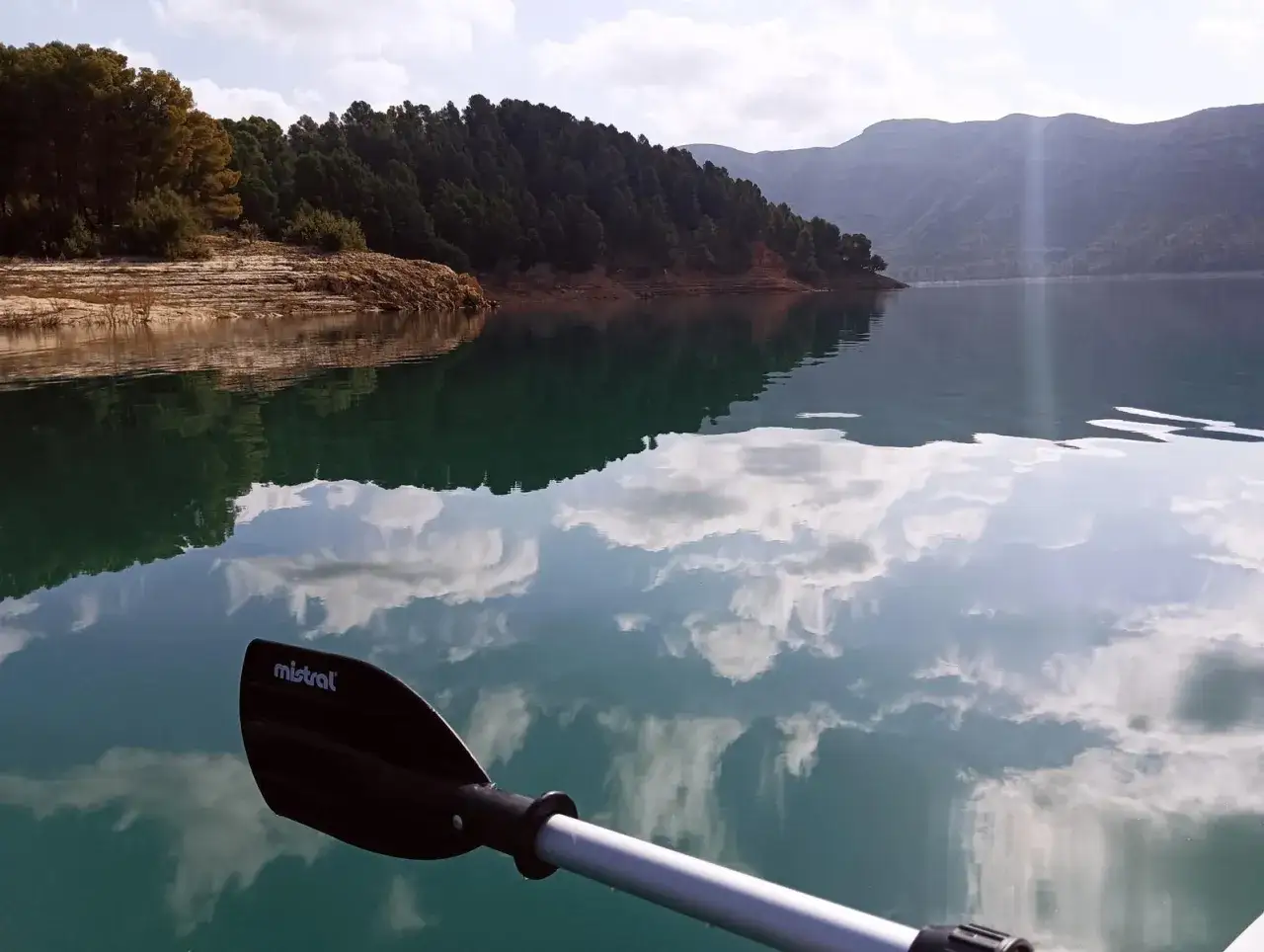 Remando en el embalse de Benag&eacute;ber, con reflejos de nubes y monta&ntilde;as en el agua turquesa.