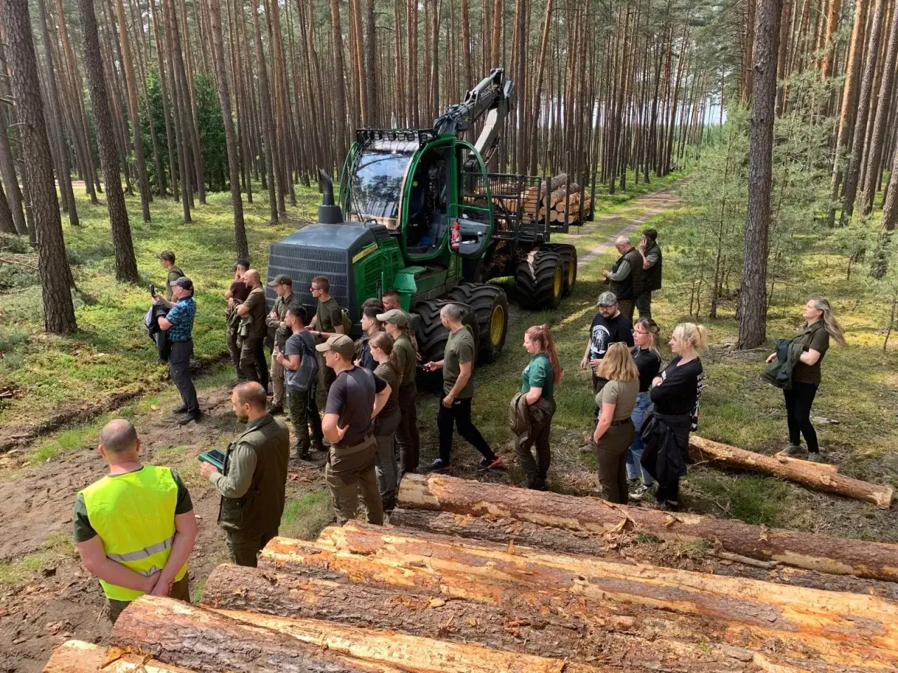 Grupa osób na leśnej polanie, przyglądająca się maszynie leśnej. To część praktycznych zajęć w ramach studiów leśniczych.