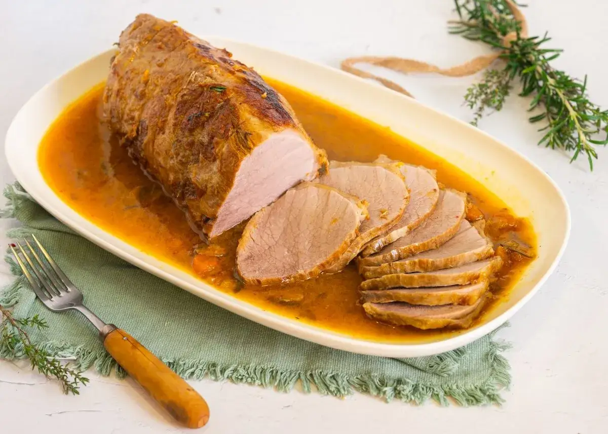 Cerdo redondo en salsa dorada, jugoso y tierno, servido en una bandeja ovalada con rodajas perfectas.