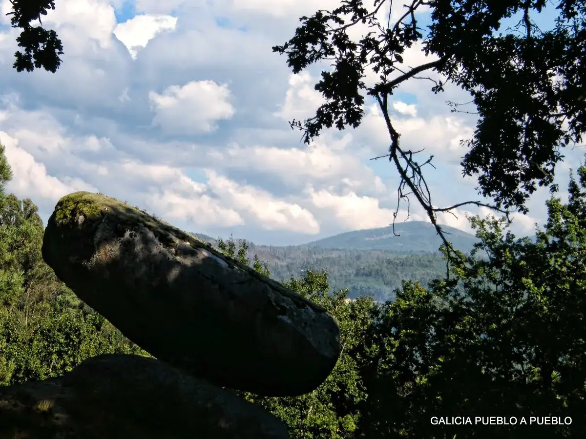 Una roca gigante en un precario **pena do equilibrio** se alza sobre un paisaje verde y monta&ntilde;oso, bajo un cielo nublado.
